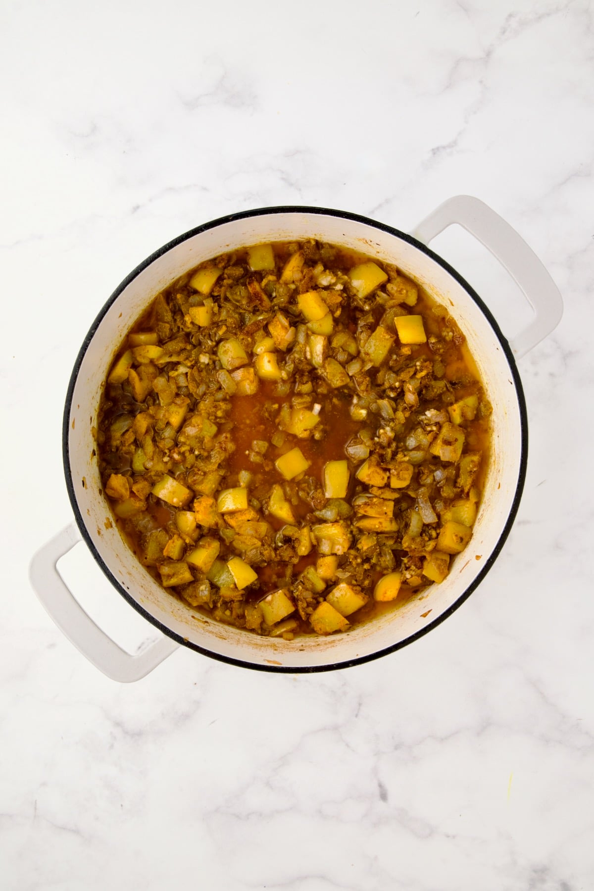 Broth added to sauteed spices, onions and yellow bell pepper in white enamel cast iron skillet.