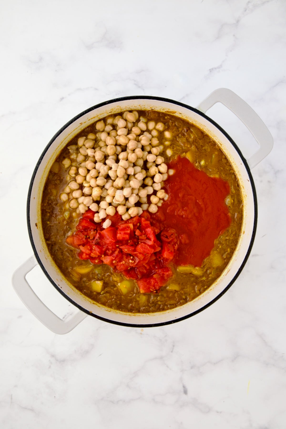 Chickpeas, diced tomatoes and tomato sauce added to onions, yellow bell pepper and spices in white enamel cast iron skillet.