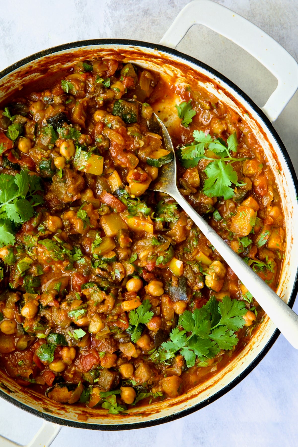 Finished Moroccan Eggplant Stew in white enamel cast iron skillet with large mixing spoon.