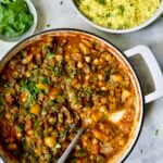 Finished Moroccan Eggplant Stew in white enamel cast iron skillet with bowl of couscous.