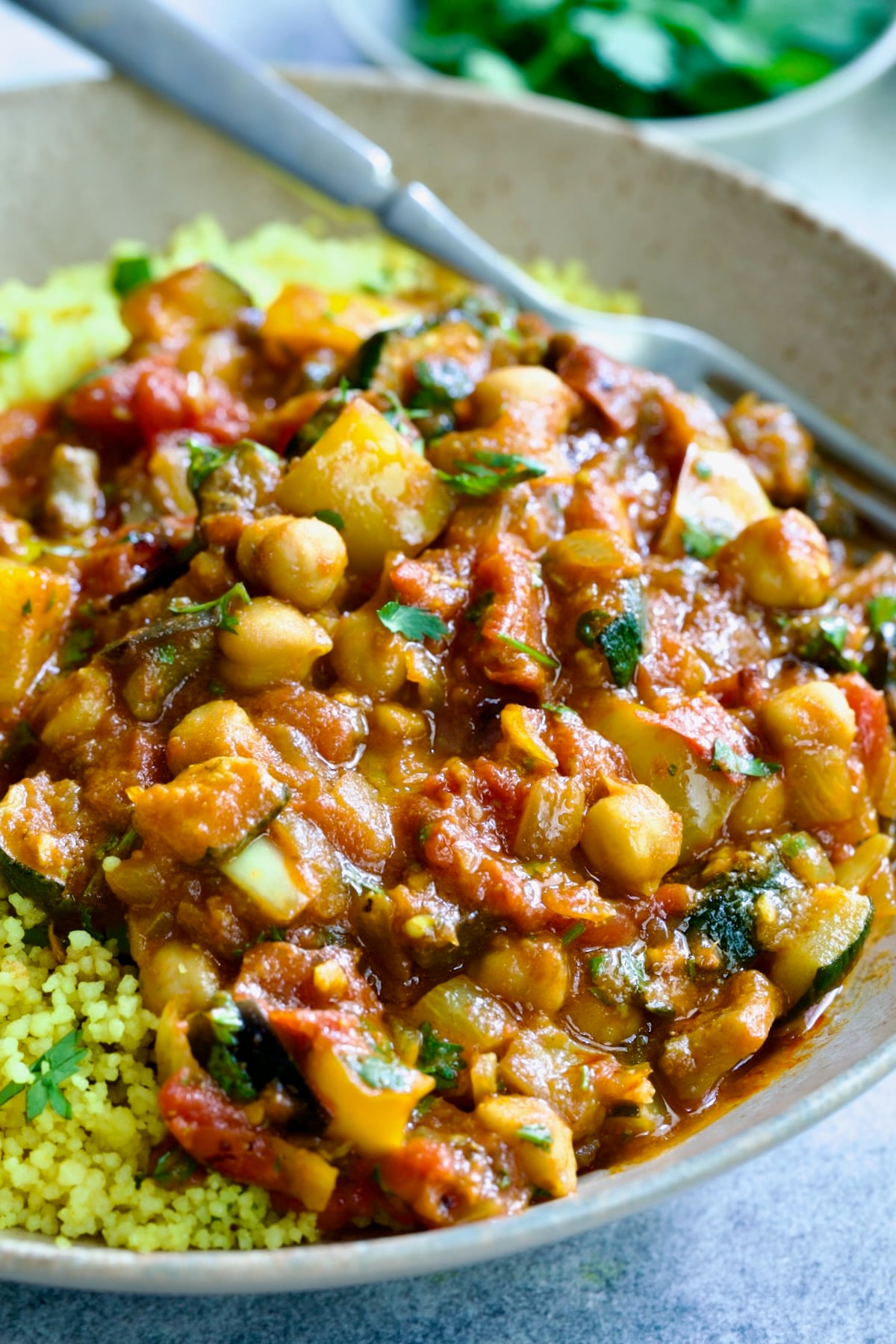 One serving of Moroccan Eggplant Stew and couscous in earthenware bowl with dinner fork.
