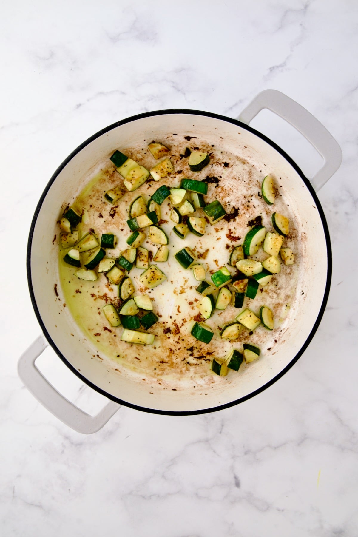 Sauteed cubed zucchini in white enamel cast iron skillet.