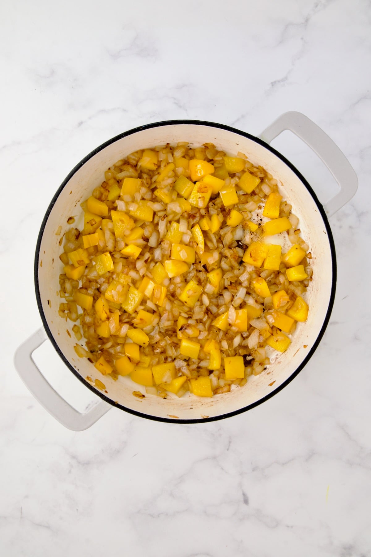 Sauteed onion and yellow bell pepper in white enamel cast iron skillet.