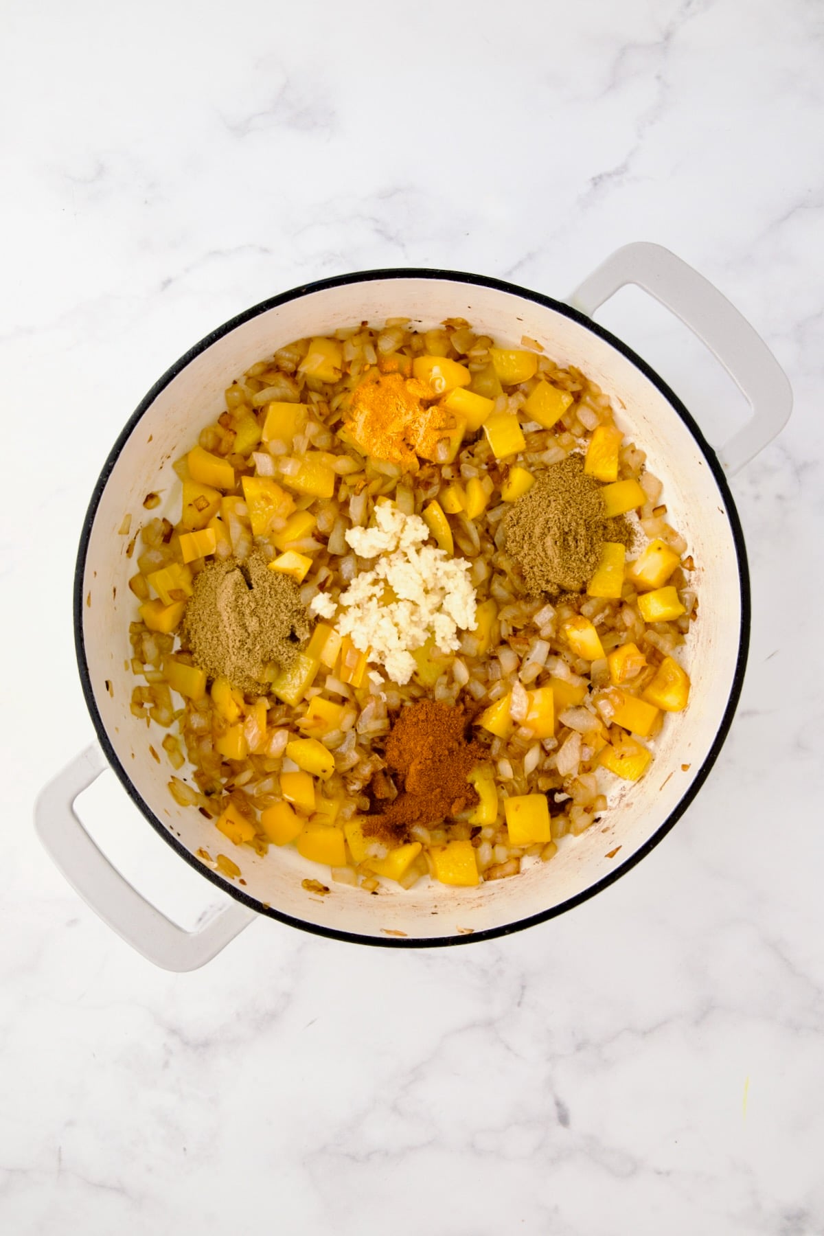 Spices and garlic added to onions and yellow bell pepper in white enamel cast iron skillet.