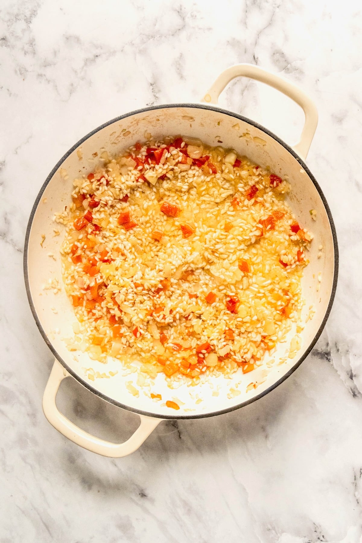 White wine added to rice, onion, and red bell pepper in white enamel cast iron skillet.