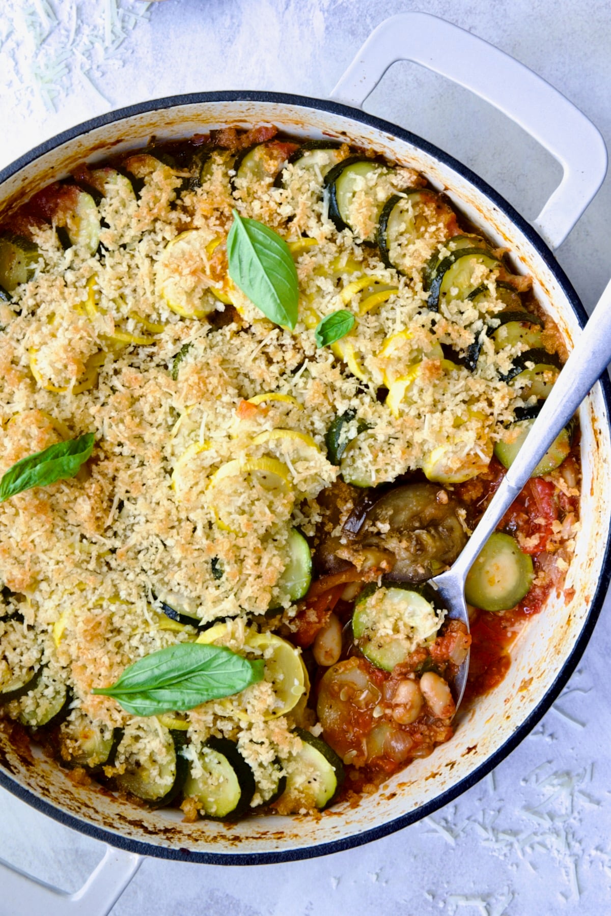 Summer Vegetable Cassoulet in white enamel cast iron skillet with serving spoon scooping some up.