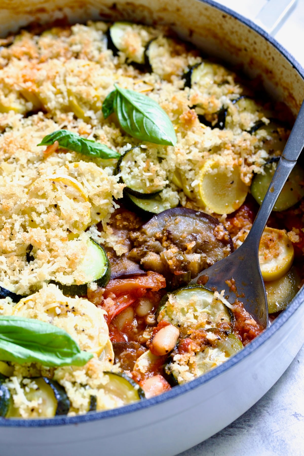 Summer Vegetable Cassoulet in white enamel cast iron skillet with serving spoon scooping some up.