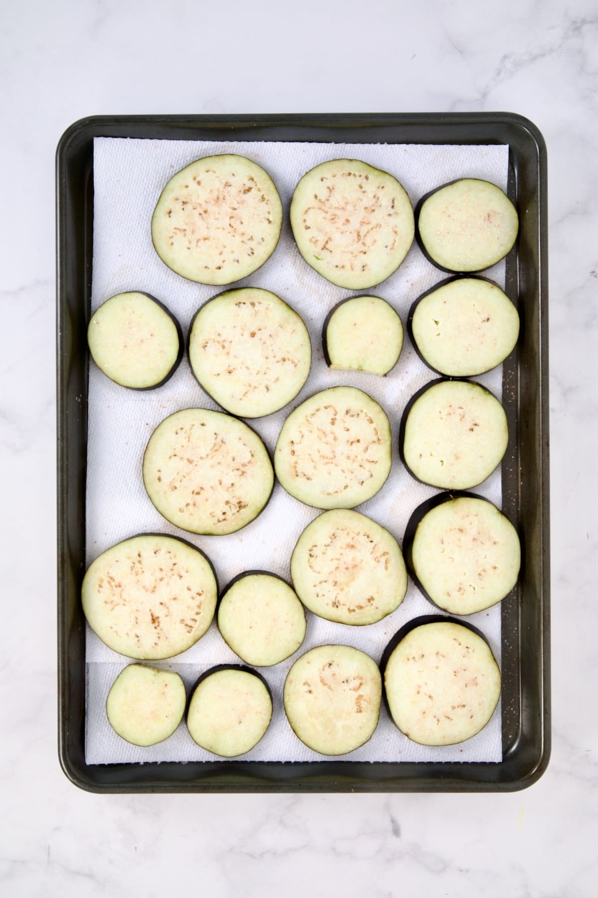 Eggplant slices on paper towel-lined rimmed baking sheet.