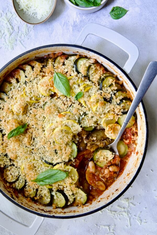Summer Vegetable Cassoulet in white enamel cast iron skillet with serving spoon scooping some up.
