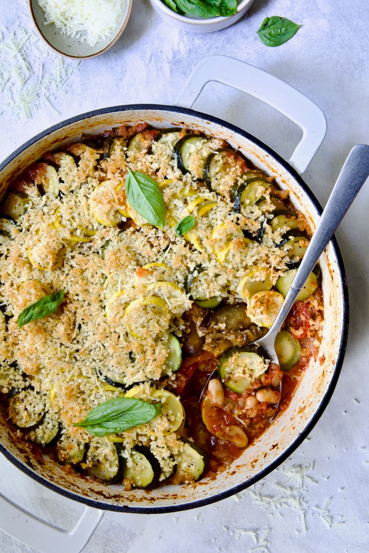Summer Vegetable Cassoulet in white enamel cast iron skillet with serving spoon scooping some up.