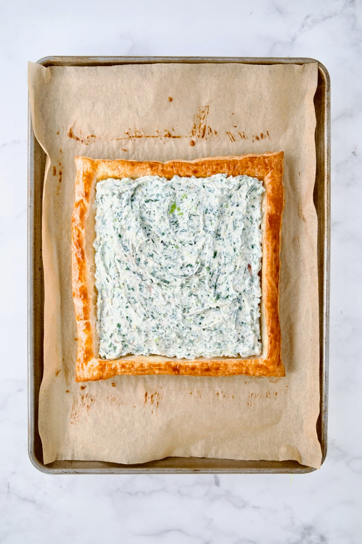 Ricotta blend spread over baked puff pastry crust on parchment paper-lined baking sheet.