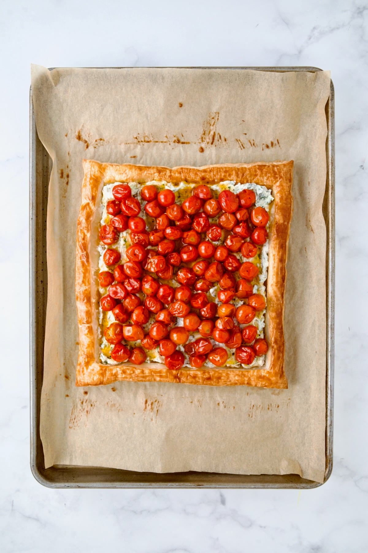 Roasted cherry tomatoes over ricotta blend on crust on parchment paper lined baking sheet.