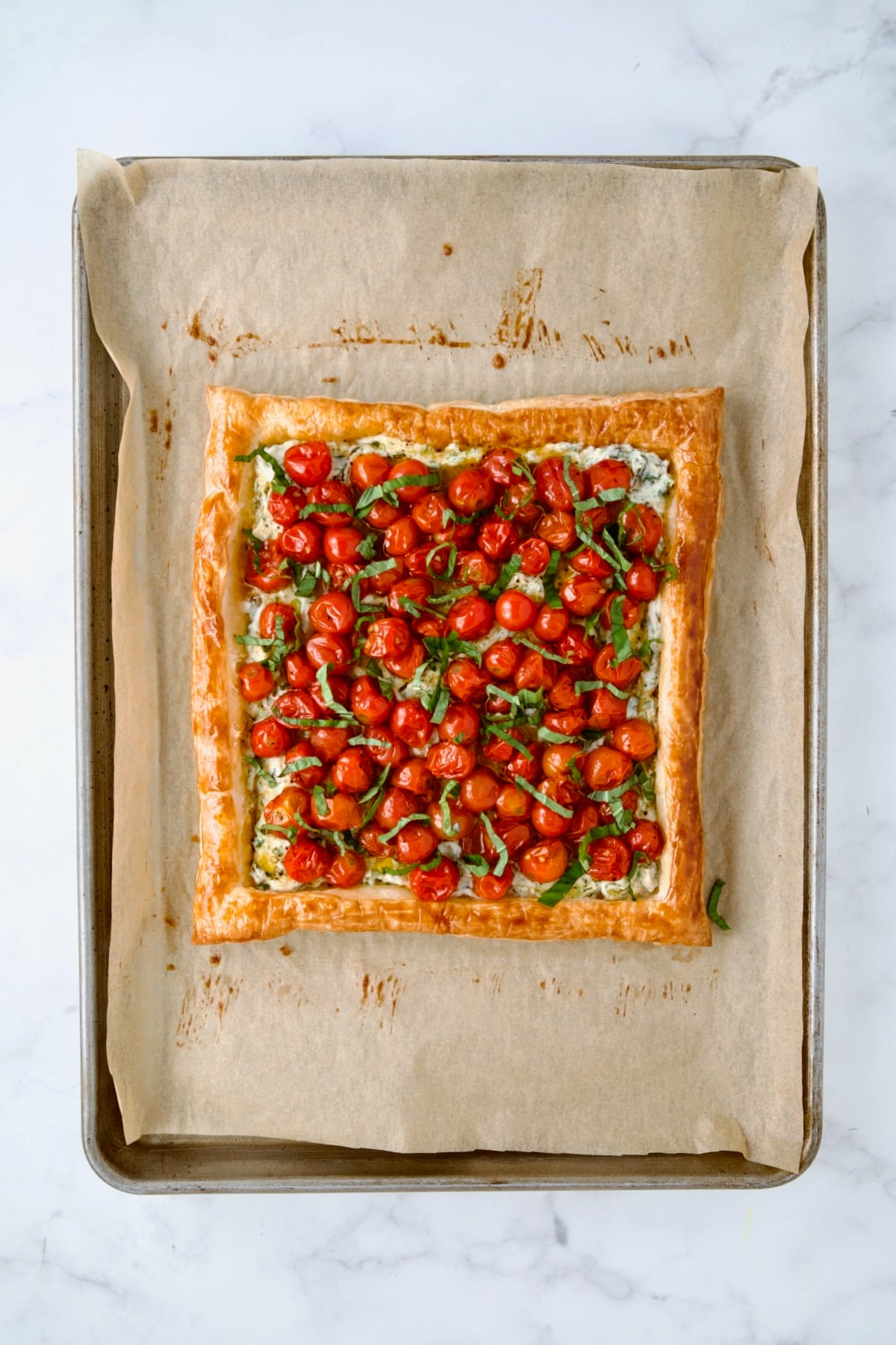 Roasted cherry tomatoes over ricotta blend on crust on parchment paper lined baking sheet with sliced basil added.