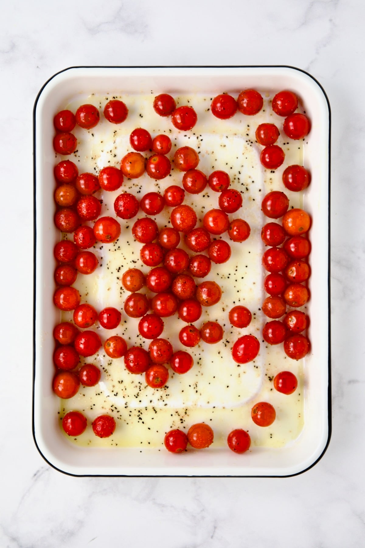 Whole cherry tomatoes in white enamel rimmed baking sheet before being roasted.