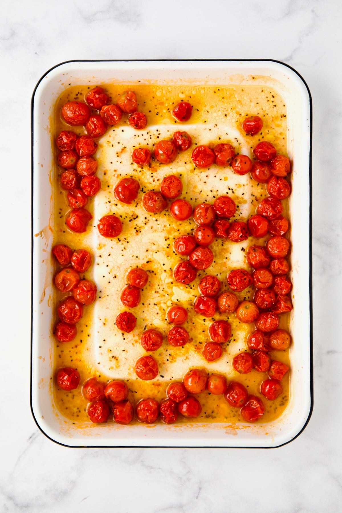 Whole cherry tomatoes in white enamel rimmed baking sheet after being roasted.