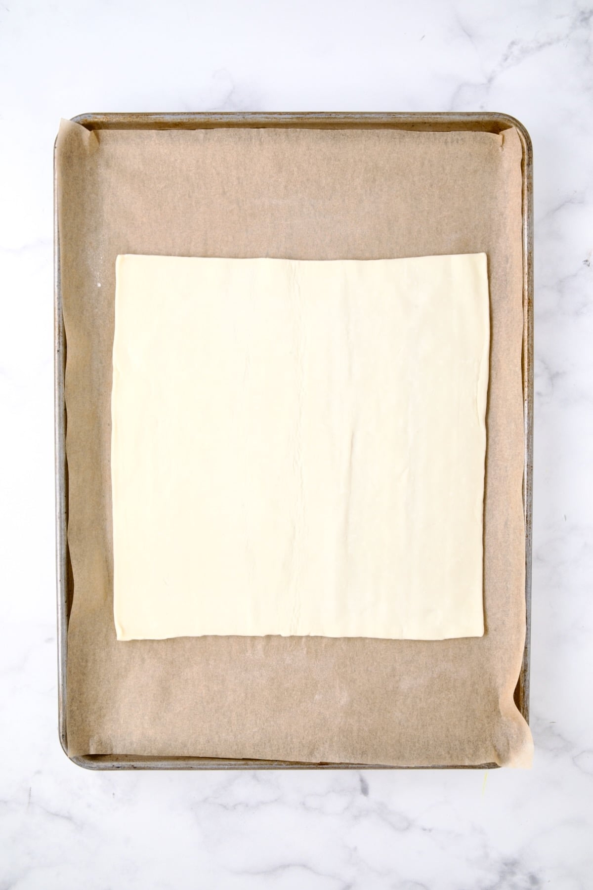 Square of puff pastry on parchment paper-lined rimmed baking sheet.