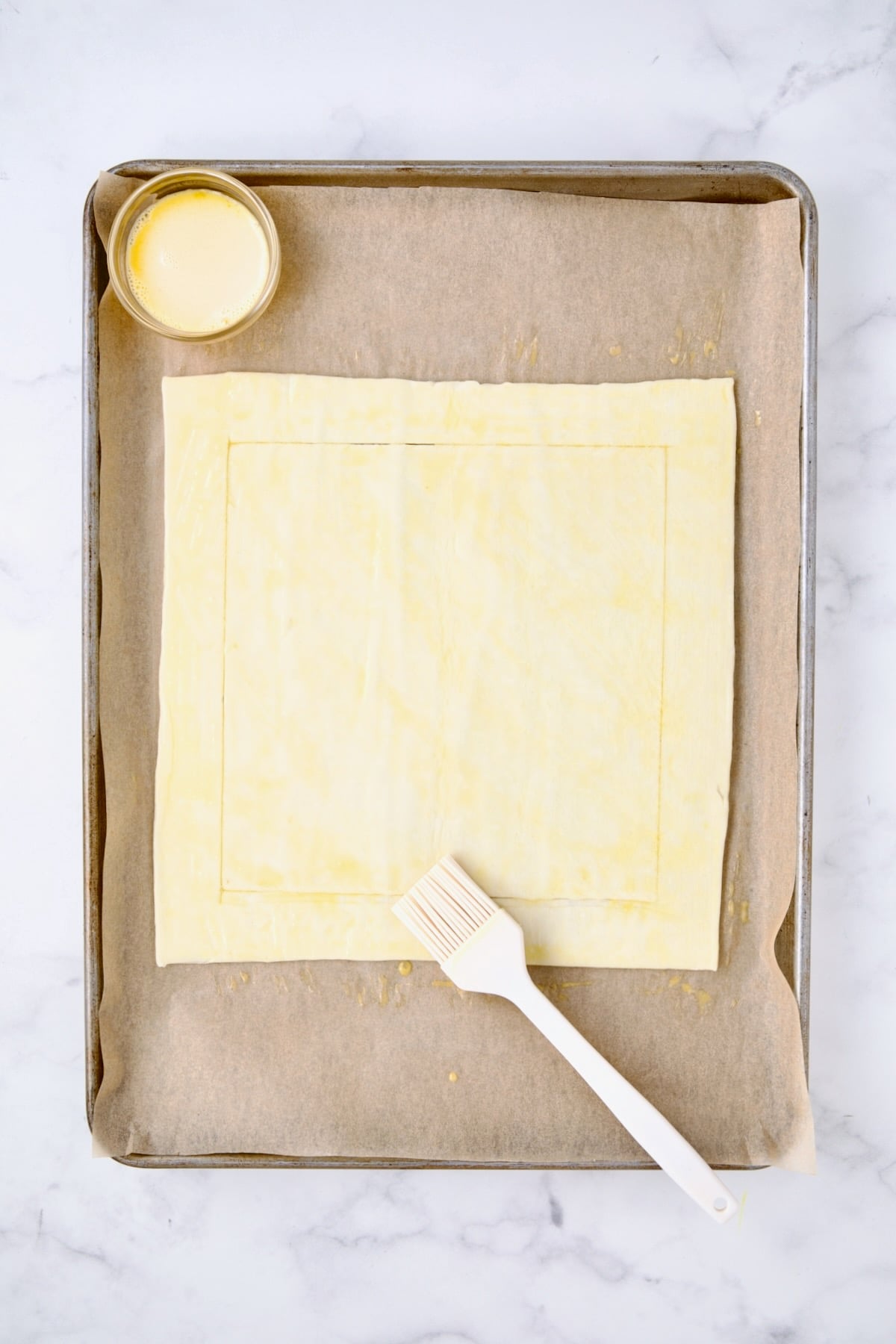 Scored puff pastry square being brushed with egg wash.