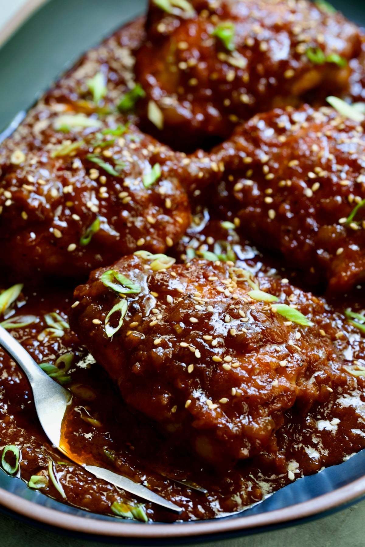 Four Korean Chicken Thighs on black oval platter with serving fork.