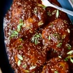 Four Korean Chicken Thighs on black oval platter with serving fork.