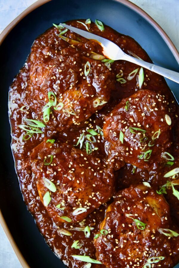 Four Korean Chicken Thighs on black oval platter with serving fork.