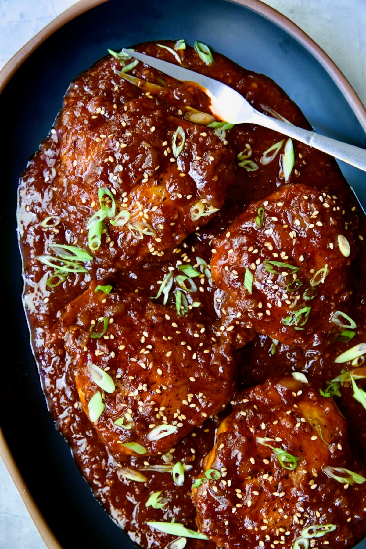 Four Korean Chicken Thighs on black oval platter with serving fork.