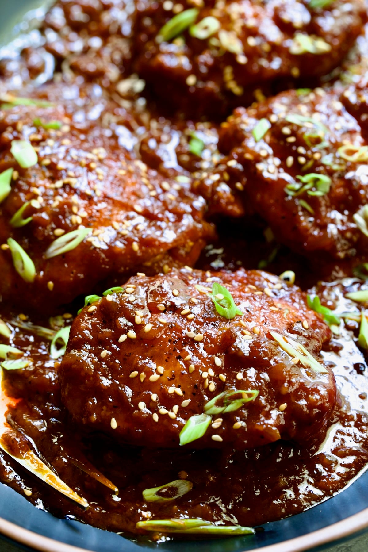Four Korean Chicken Thighs on black oval platter with serving fork.