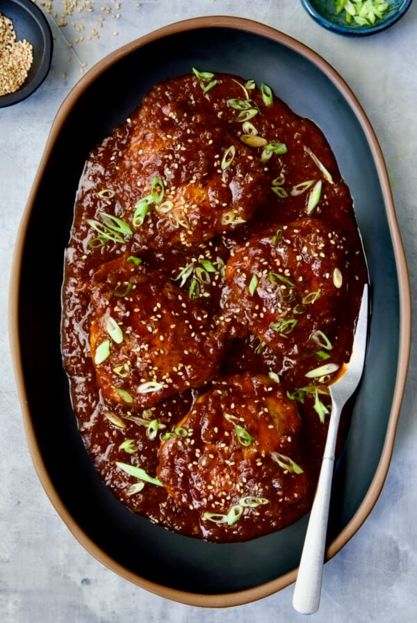 Four Korean Chicken Thighs on black oval platter with serving fork.