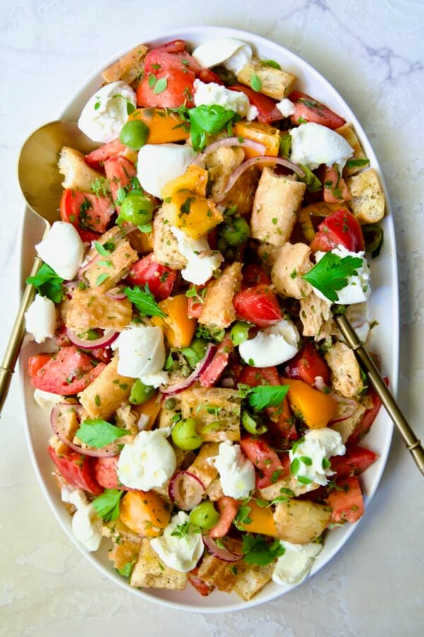 Panzanella with Preserved Lemon Viniagrette on oval white platter with gold serving utensils.