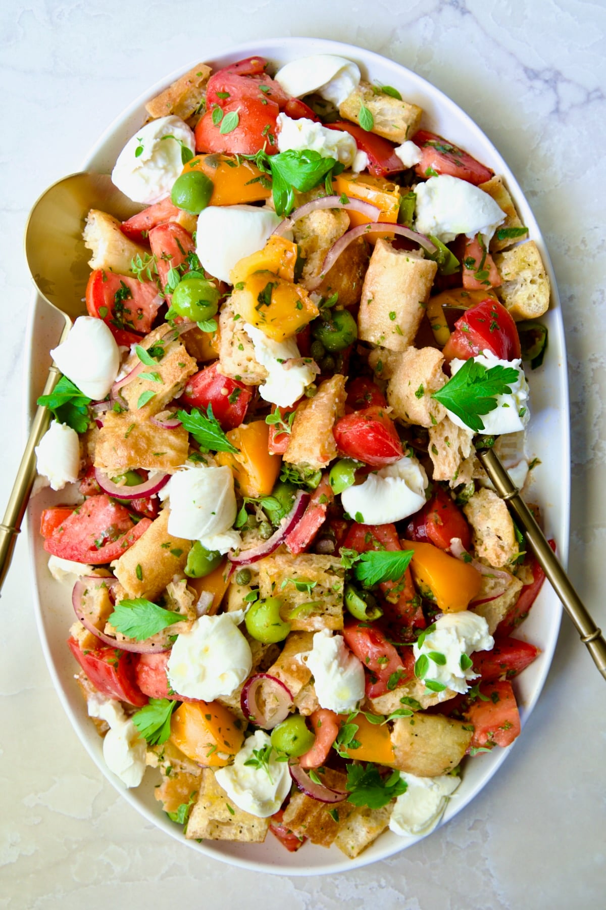 Panzanella with Preserved Lemon Viniagrette on oval white platter with gold serving utensils.