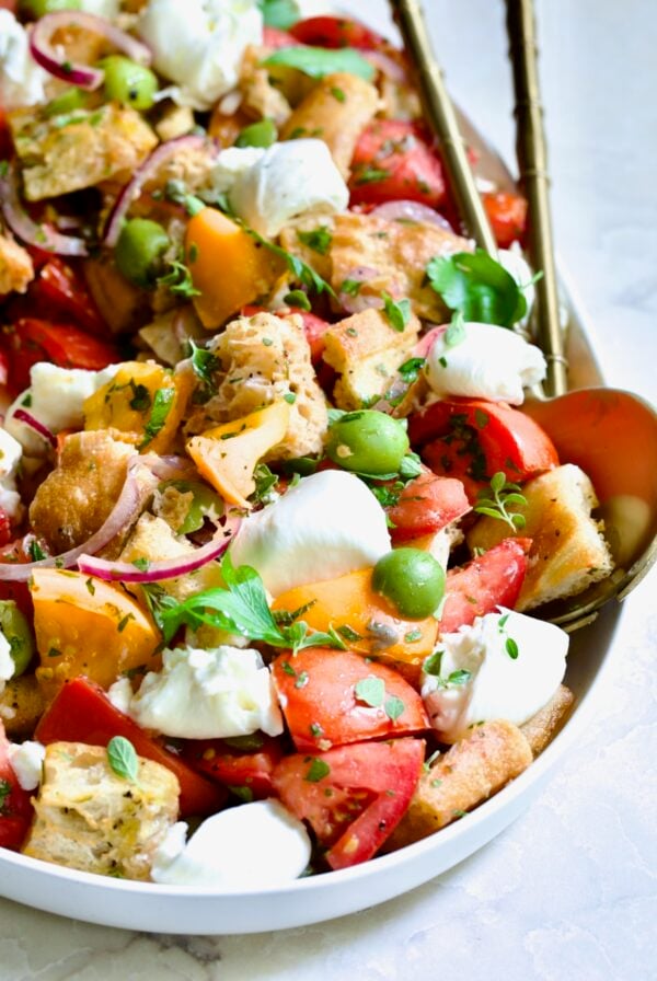 Panzanella with Preserved Lemon Viniagrette on oval white platter with gold serving utensils.