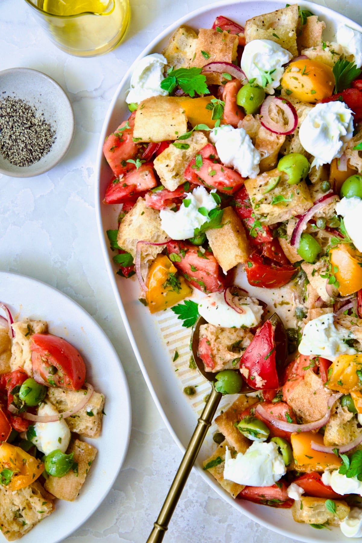 Panzanella with Preserved Lemon Viniagrette on oval white platter with some served on round white plate.