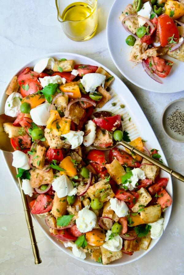 Panzanella with Preserved Lemon Viniagrette on oval white platter with some served on round white plate.