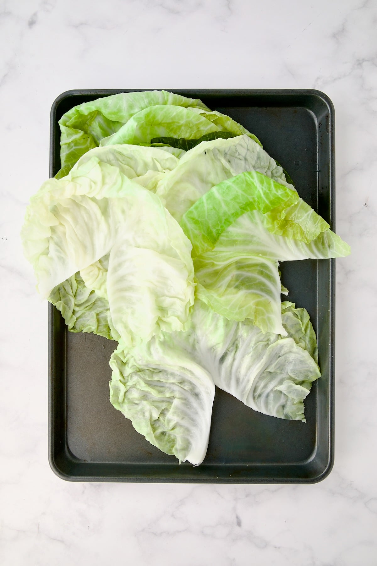 Cabbage leaves on rimmed sheet pan with stem rib removed.