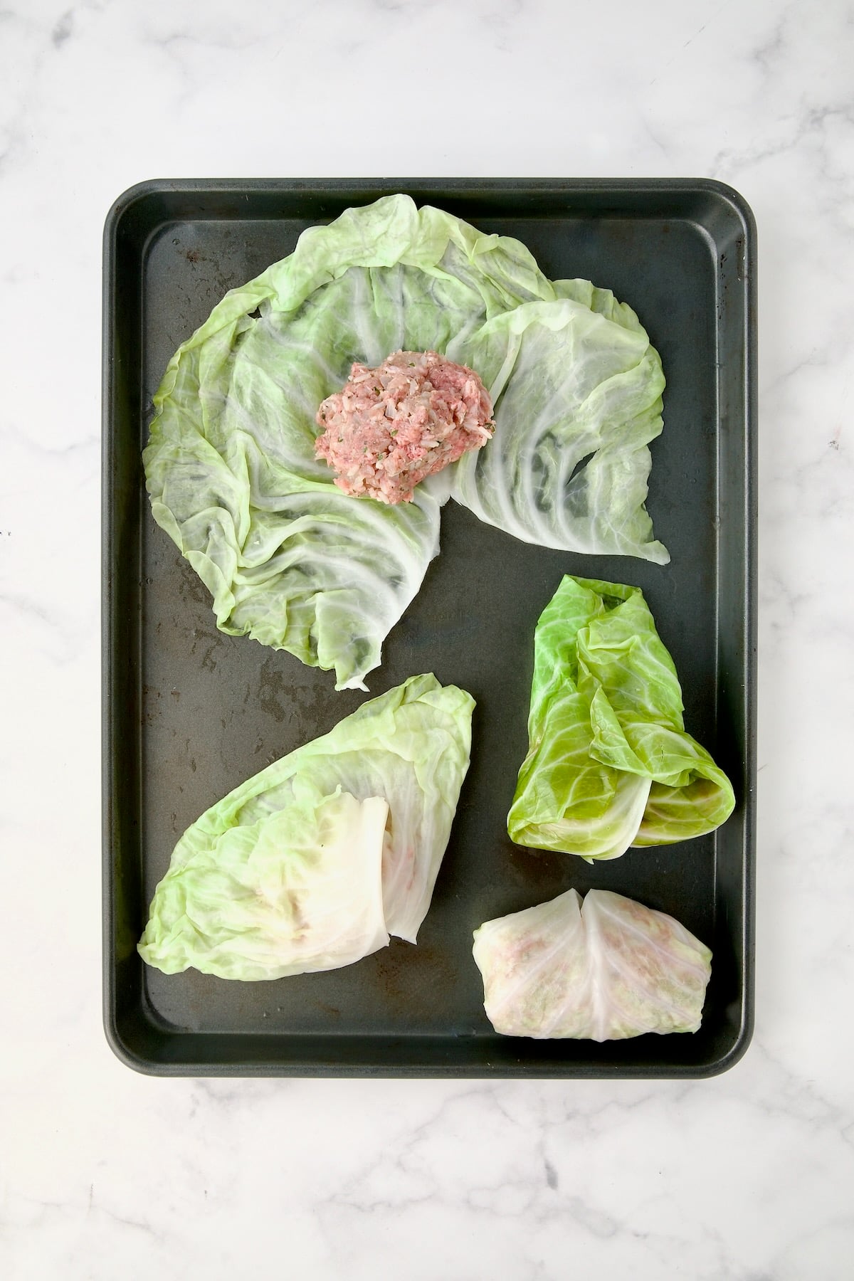 Cabbage leaves on rimmed sheet pan showing how to roll the rolls.