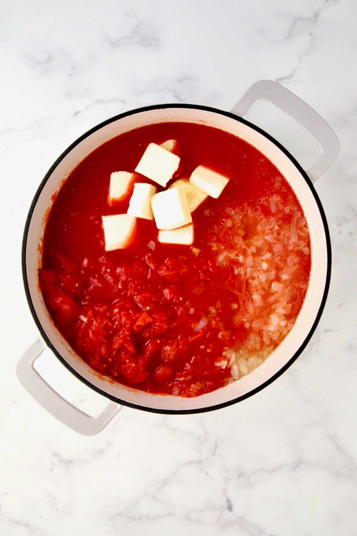 Onions, butter and tomatoes in white enamel cast iron skillet.