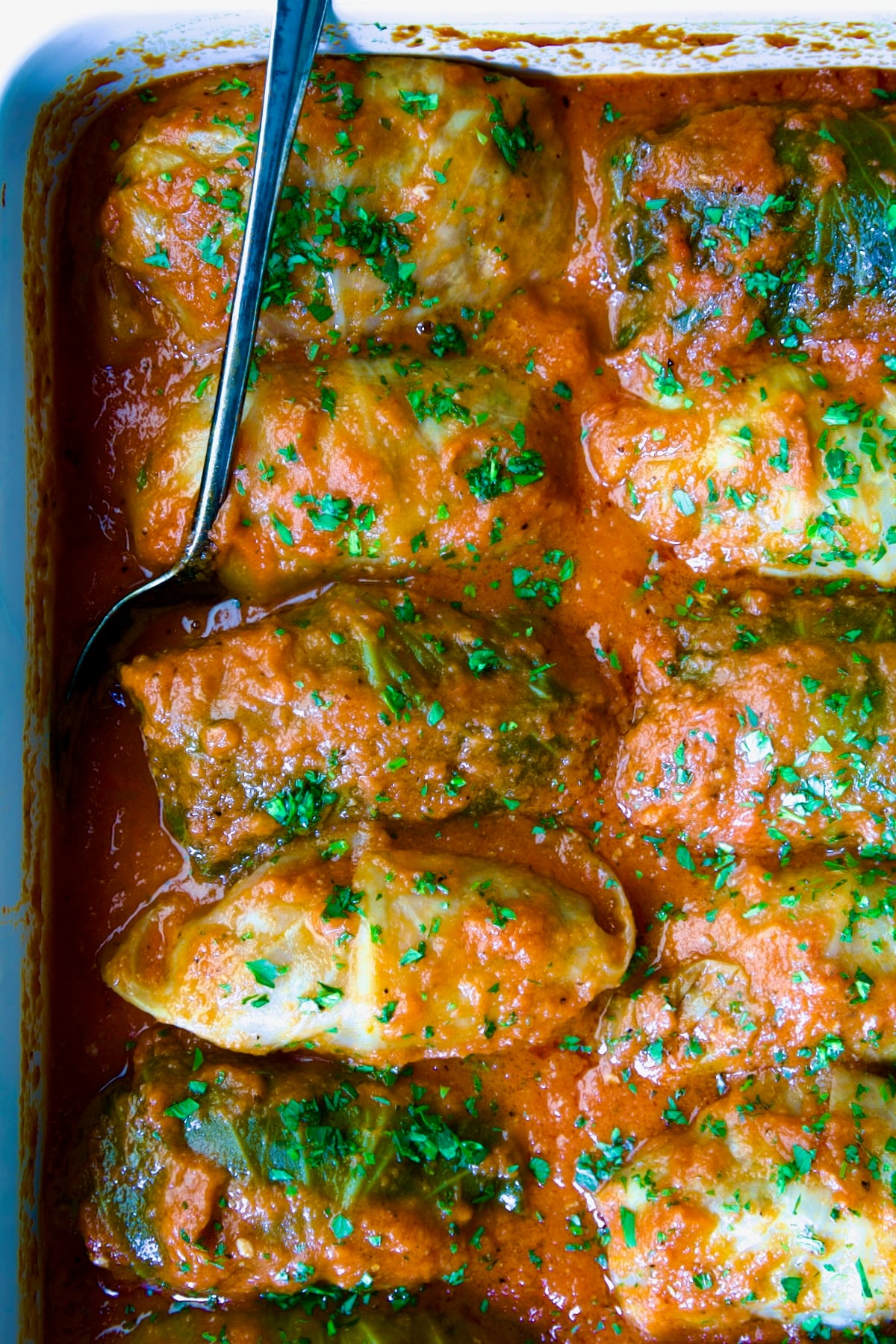 Golumpki Recipe (Polish Stuffed Cabbage) in white baking dish with serving spoon.