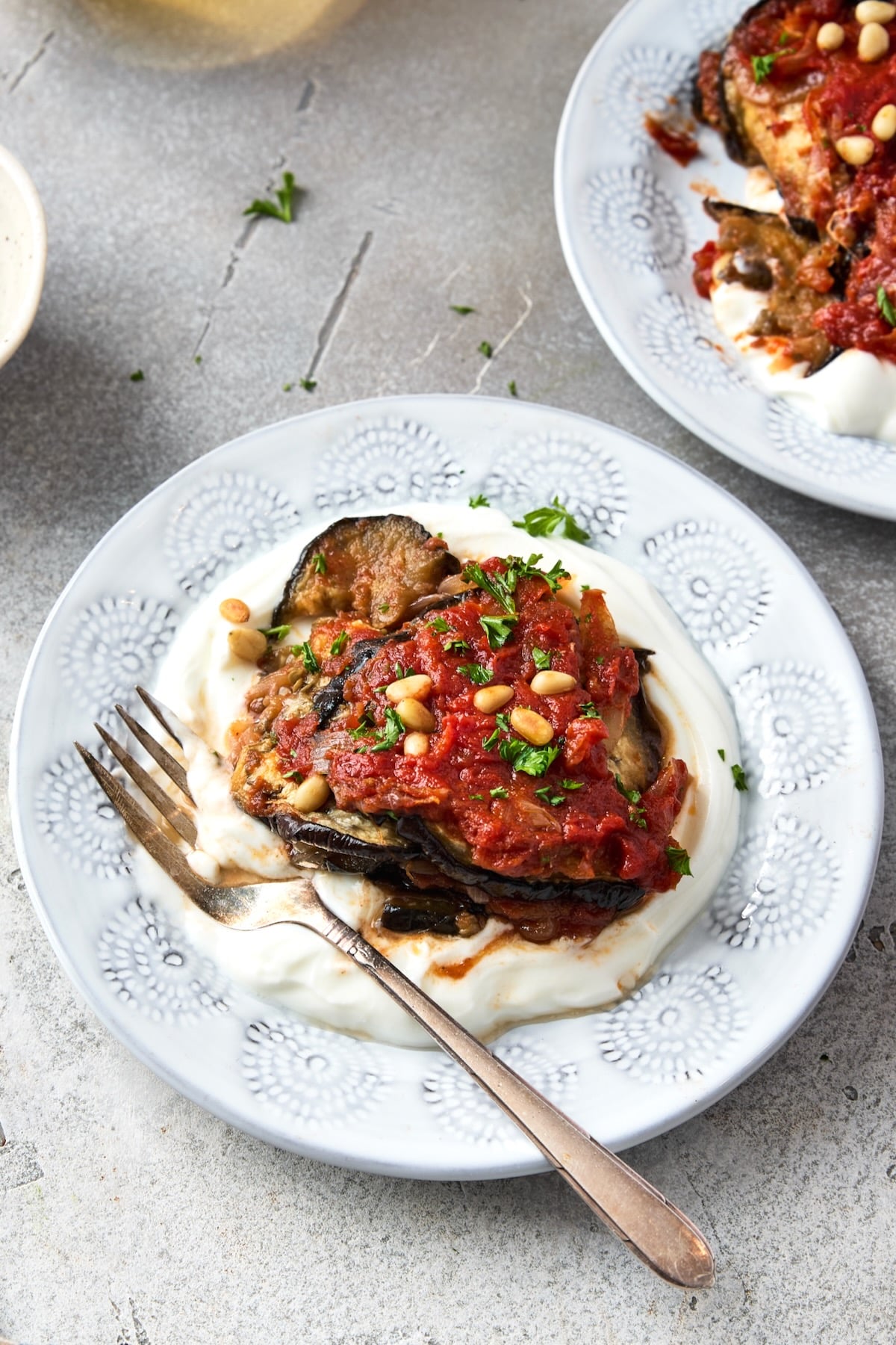 One piece of Turkish Eggplant Casserole over yogurt on white decorative plate.