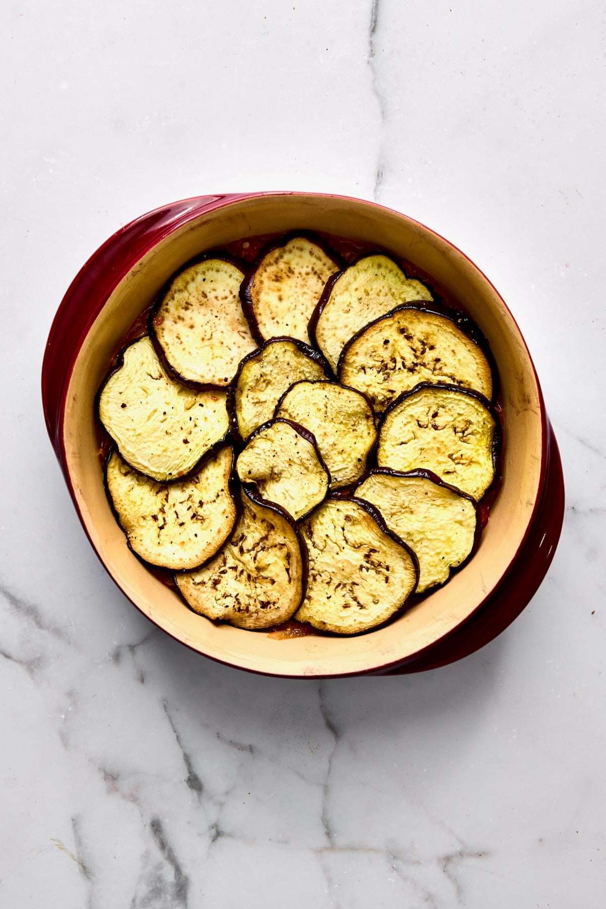 Eggplant placed over tomato sauce in round baking dish.