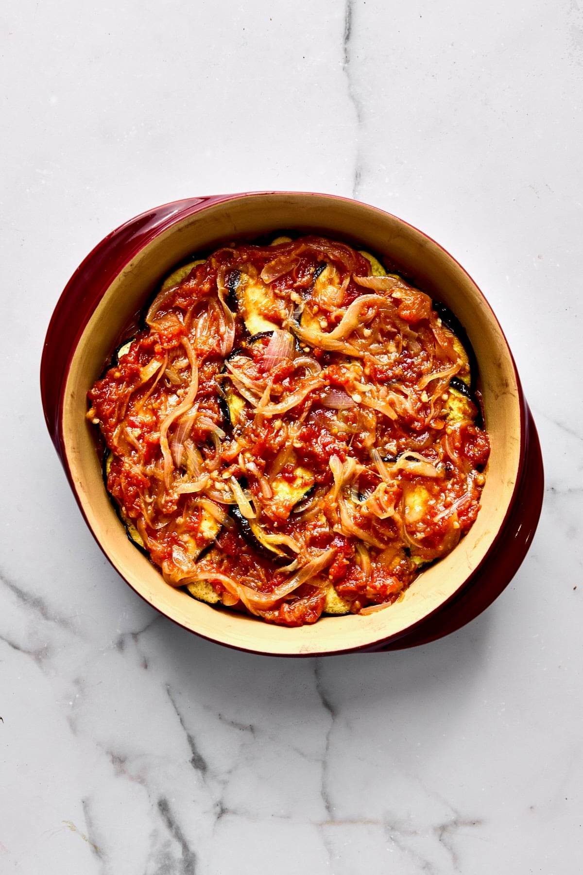 Tomato sauce over eggplant in round baking dish.