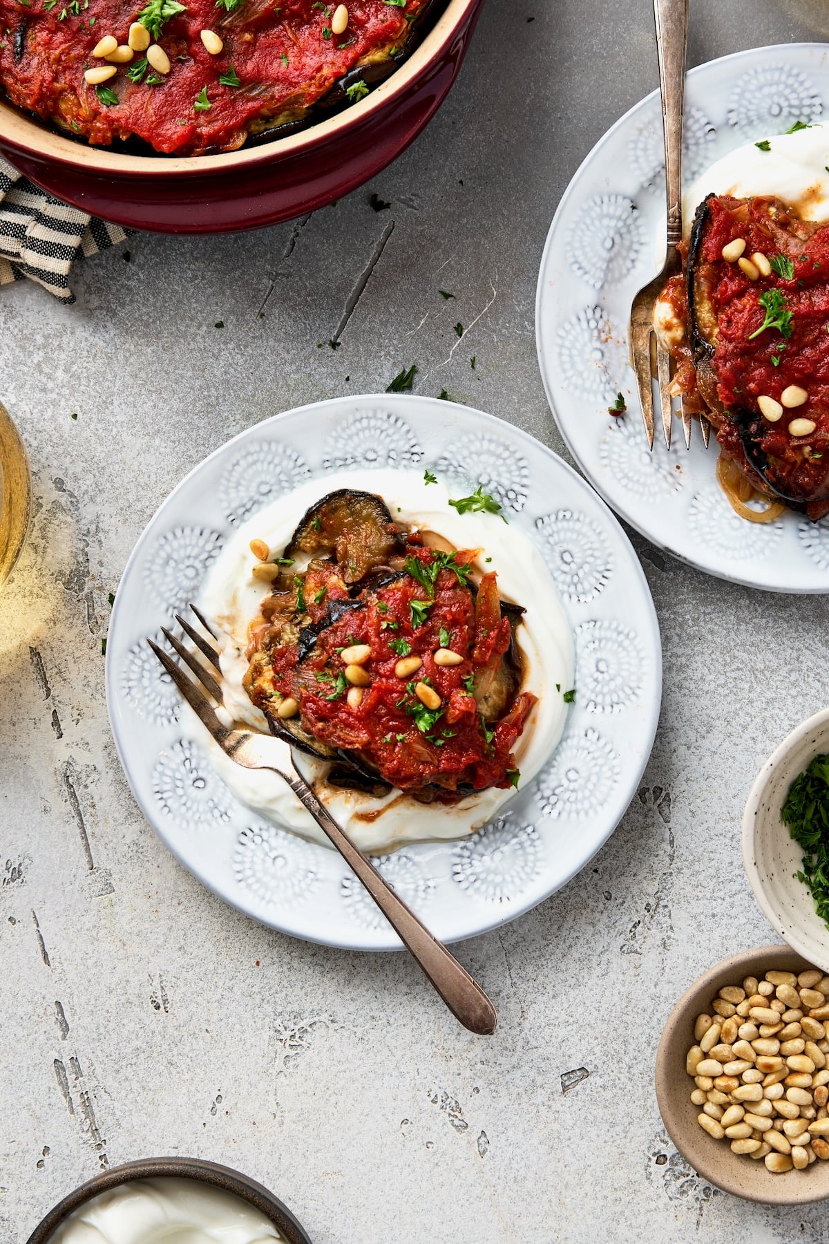 One piece of Turkish Eggplant Casserole over yogurt on white decorative plate.