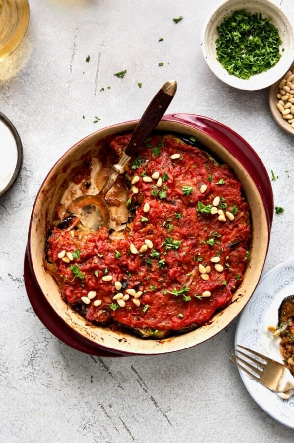 Turkish Eggplant Casserole in round red baking dish with serving utensil with a piece removed.