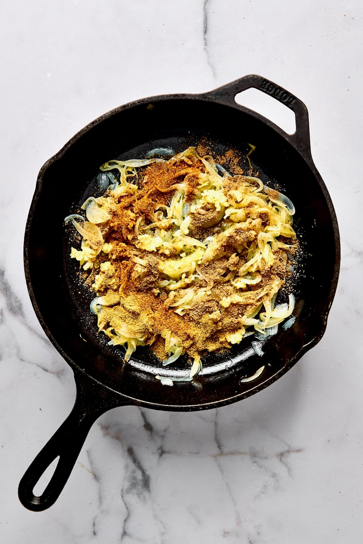 Cooked sliced onion in cast iron skillet with spices sprinkled over them.
