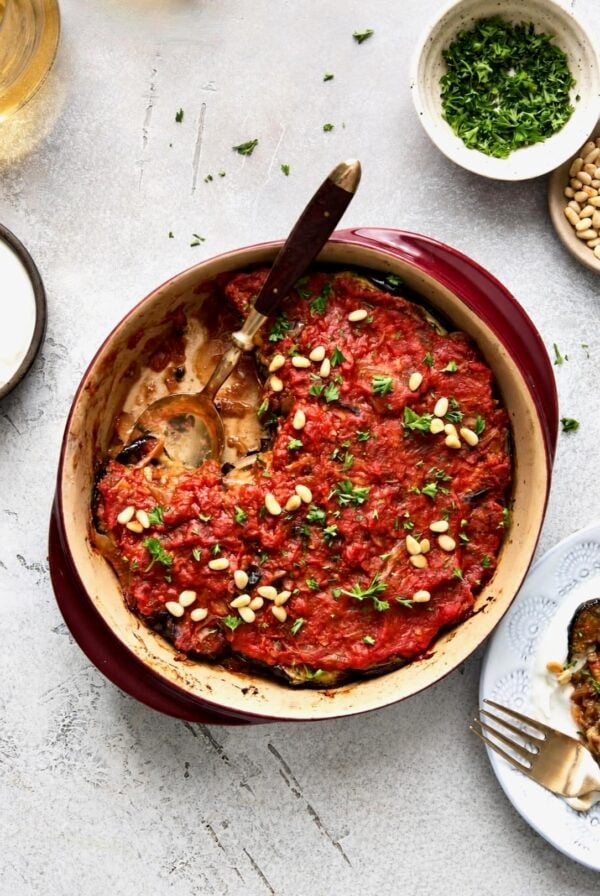 Turkish Eggplant Casserole in round red baking dish with serving utensil with a piece removed.