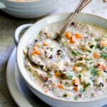 One serving of Creamy Chicken and Wild Rice Soup in white bowl with spoon.