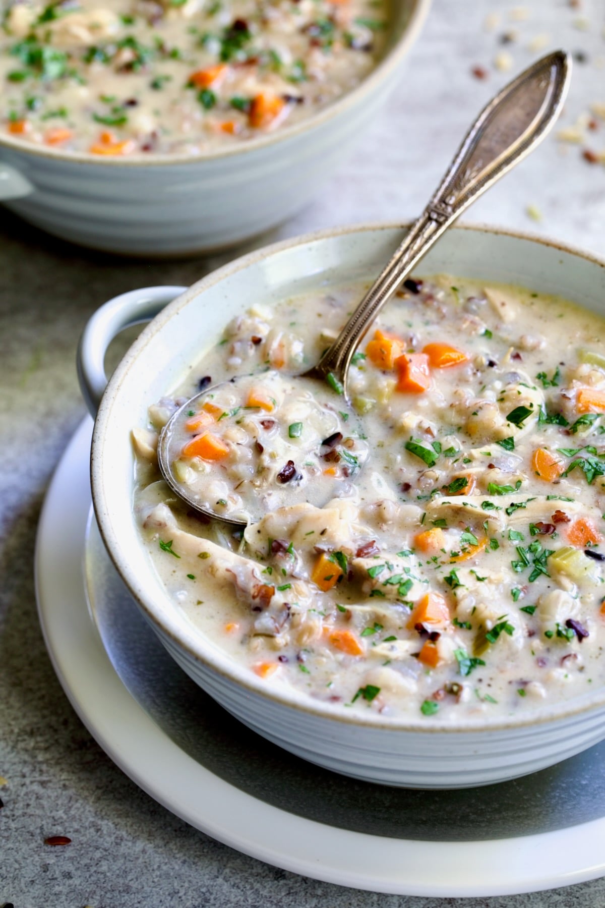 One serving of Creamy Chicken and Wild Rice Soup in white bowl with spoon.