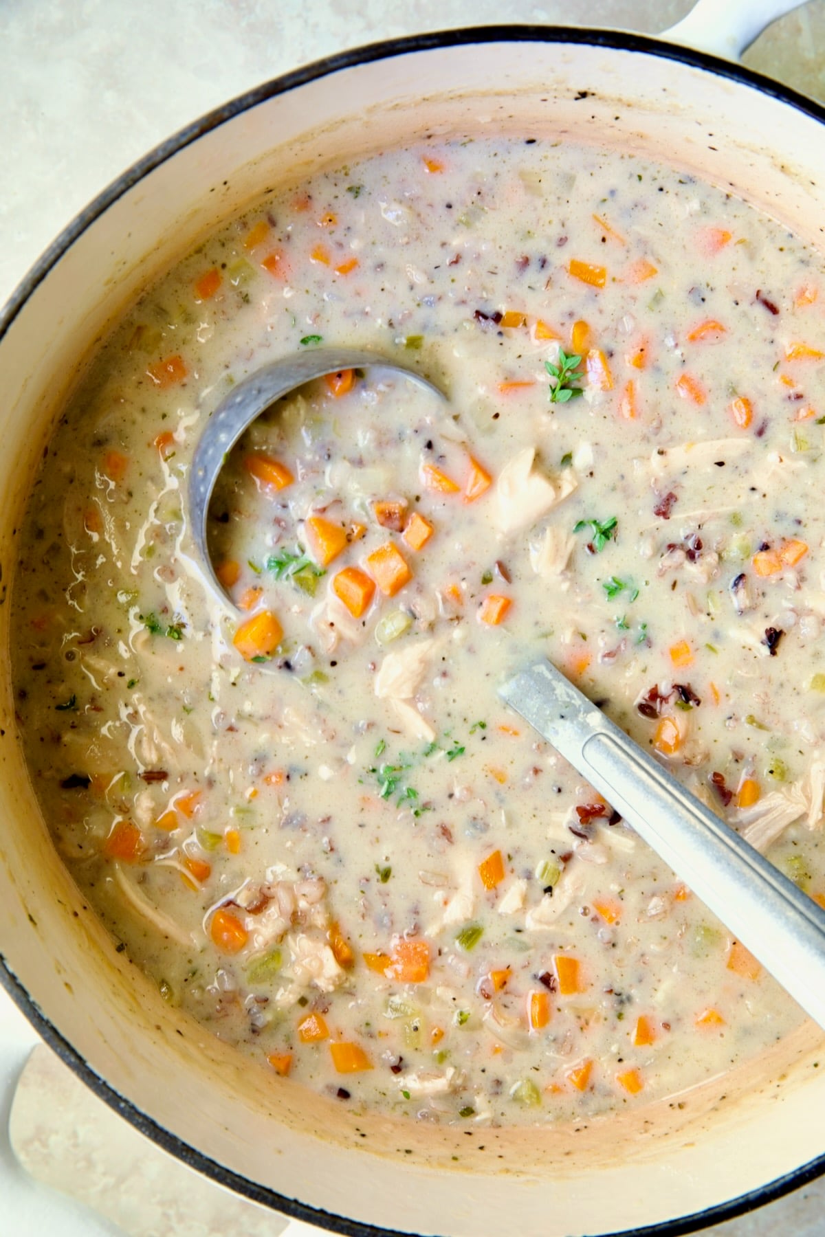 Creamy Chicken and Wild Rice Soup in white enamel Dutch oven with soup ladle.
