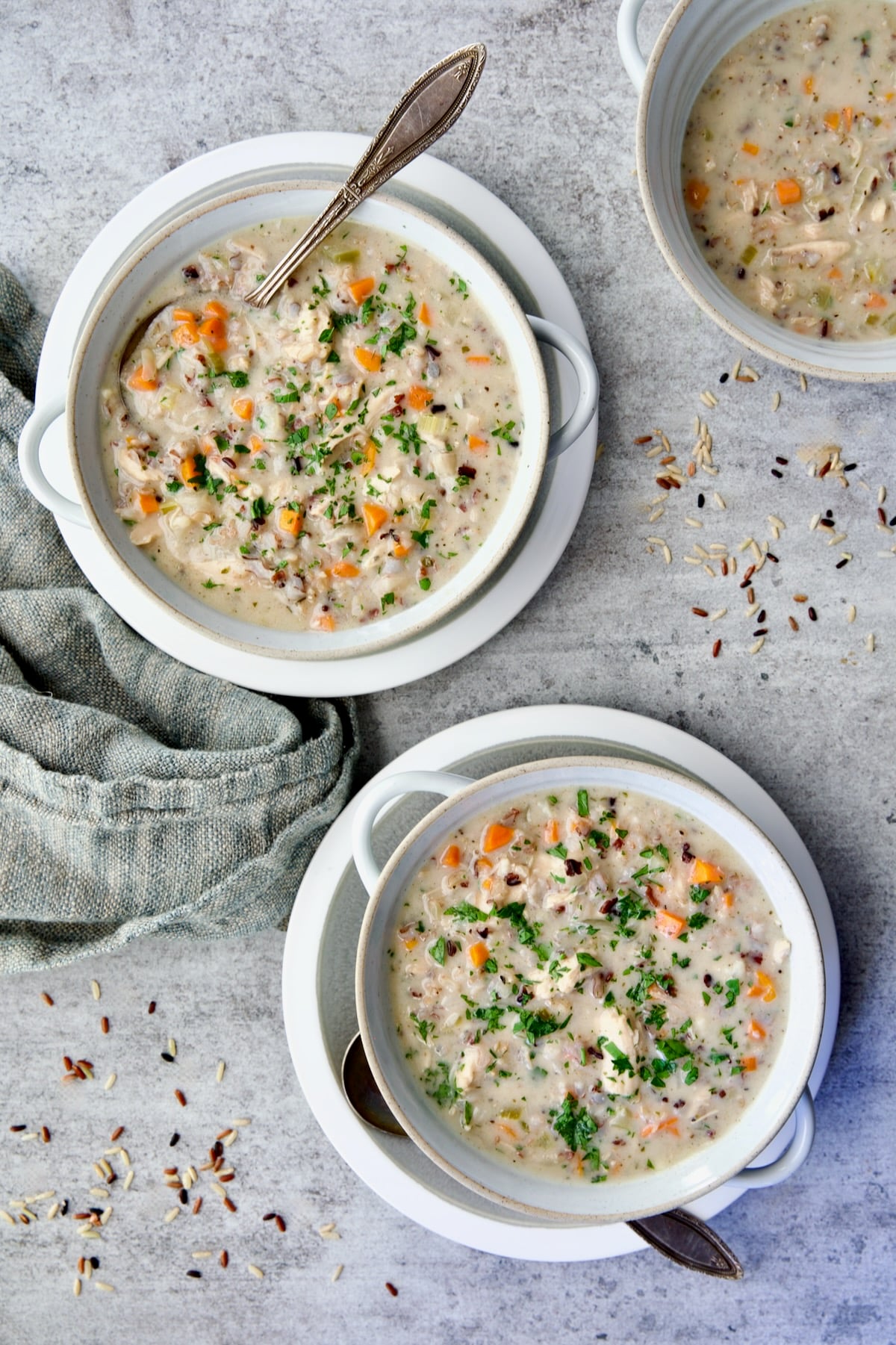 Three servings of Creamy Chicken and Wild Rice Soup in white bowl with spoon.