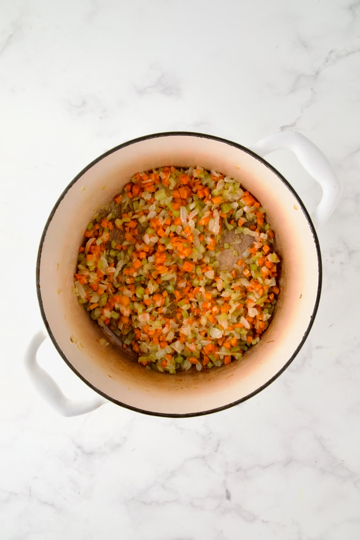 Cooked onion, carrot and celery in white enamel Dutch oven.