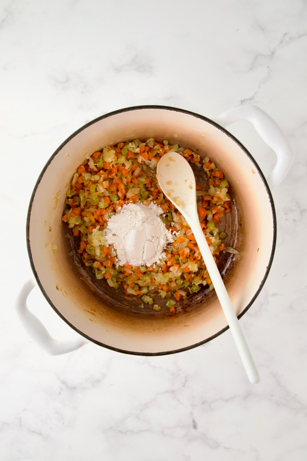Cooked onion, carrot and celery in white enamel Dutch oven with flour added.