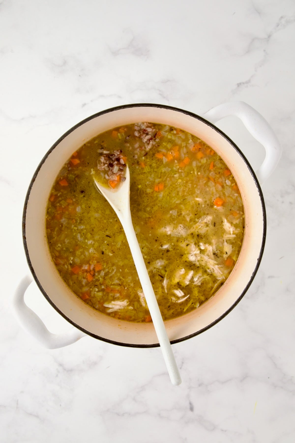 Chicken and wild rice blend added to Dutch oven with chicken broth and vegetables.